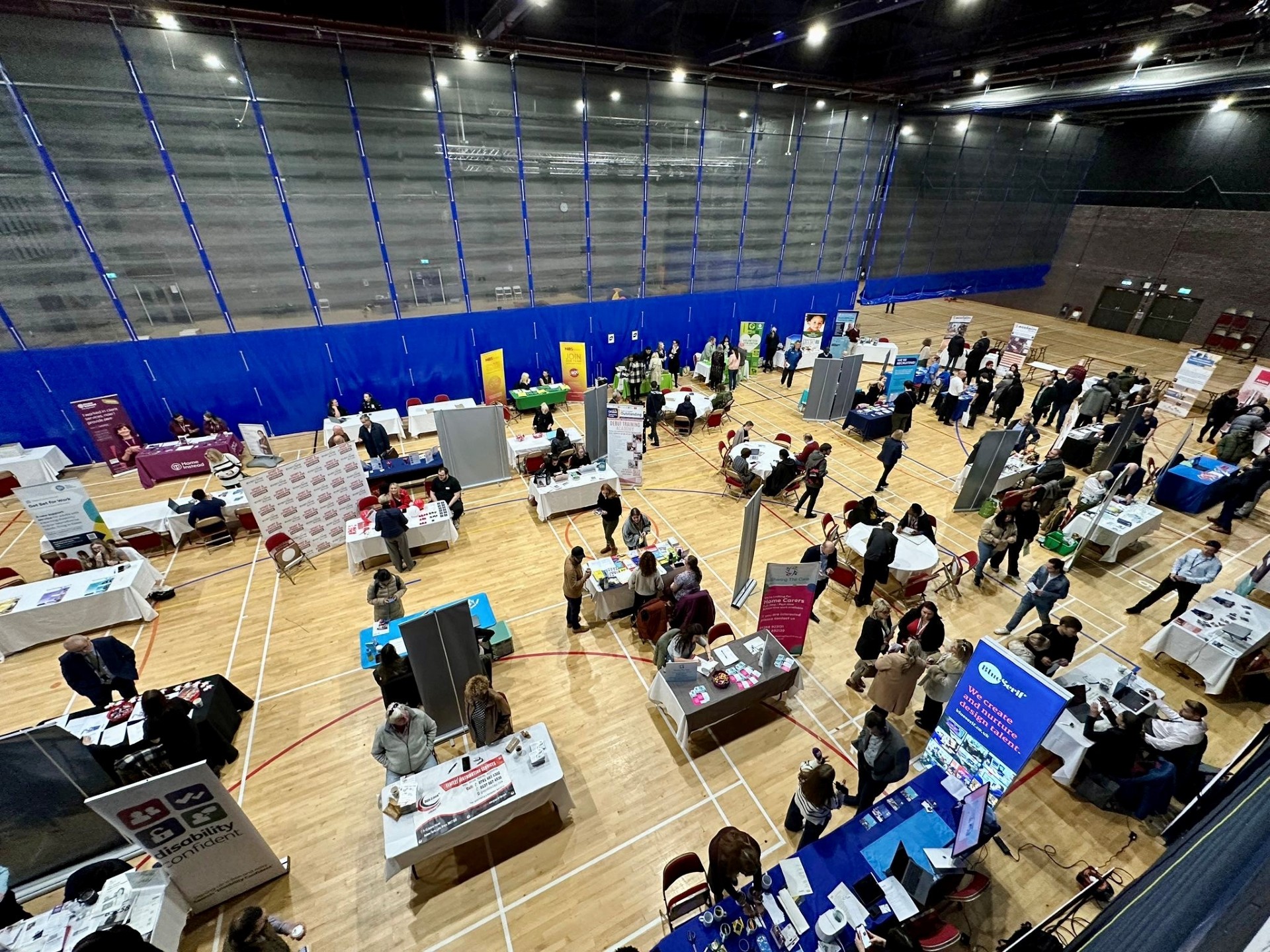 Crowded indoor job fair with booths and attendees.