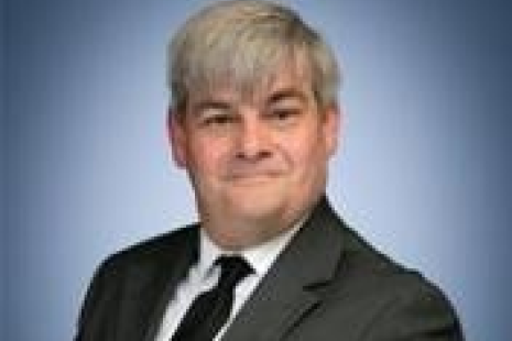 cllr Mark Reed in a suit smiling with a blue background